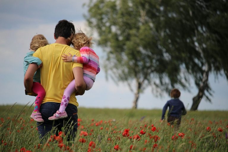 Hombre con dos niños en brazos y un niño corriendo por un campo de tulipanes rojos